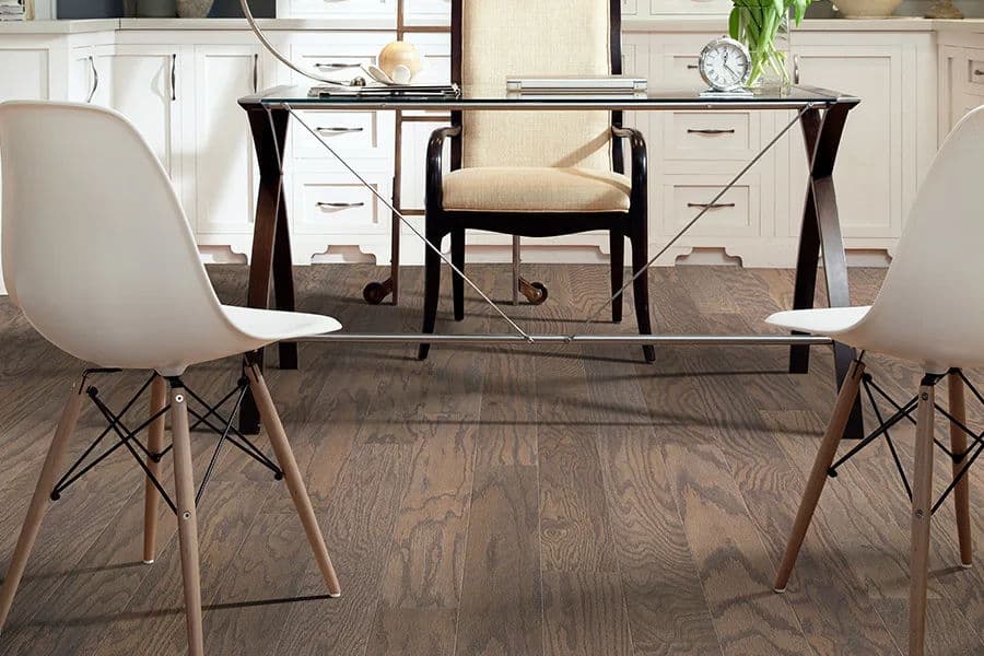 Modern office setup featuring a glass-top desk, two stylish chairs, and wooden flooring.