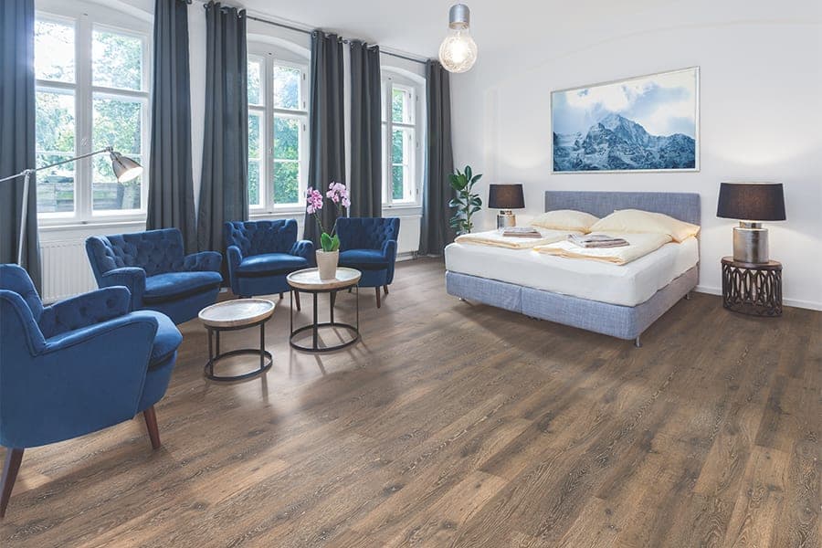 Elegant hotel room with blue chairs, a large bed, wooden floor, and mountain artwork.