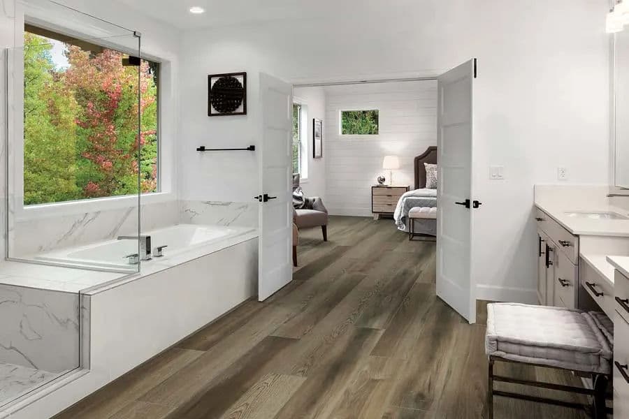 Modern bathroom with a freestanding tub, dual sinks, and wooden flooring, featuring natural light.